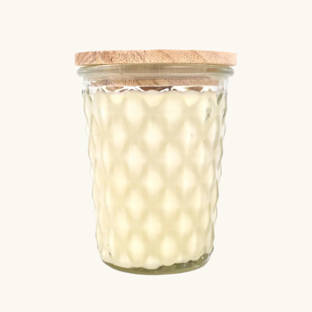 A clear glass jar candle with a textured honeycomb pattern, filled with creamy off-white wax and topped with a light natural wood lid, shown against a solid off-white background.