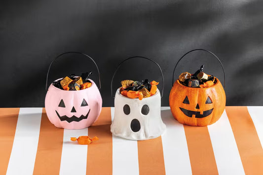 Three Halloween-themed candy buckets on a striped tablecloth with a blackboard background.