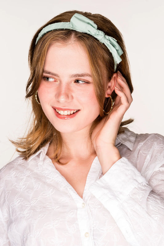 Woman wearing a mint green bow headband with knotted detail