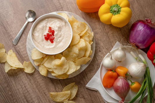 Pretzel chips with dip on a plate, surrounded by fresh vegetables on a wooden table.