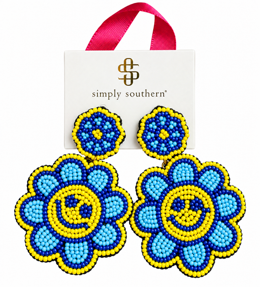 A pair of flower-shaped beaded earrings with a smiley face design, displayed in front of their white Simply Southern brand card with a pink ribbon hanger. The earrings feature light blue, royal blue, and yellow beads.