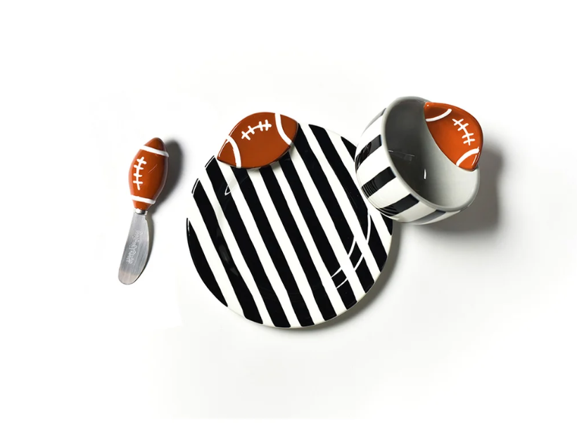 A football-themed serving set on a white background, featuring a round black and white striped plate with a football-shaped spoon resting on top, and a matching white cup with a football-shaped lid.