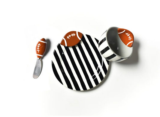 A football-themed serving set on a white background, featuring a round black and white striped plate with a football-shaped spoon resting on top, and a matching white cup with a football-shaped lid.