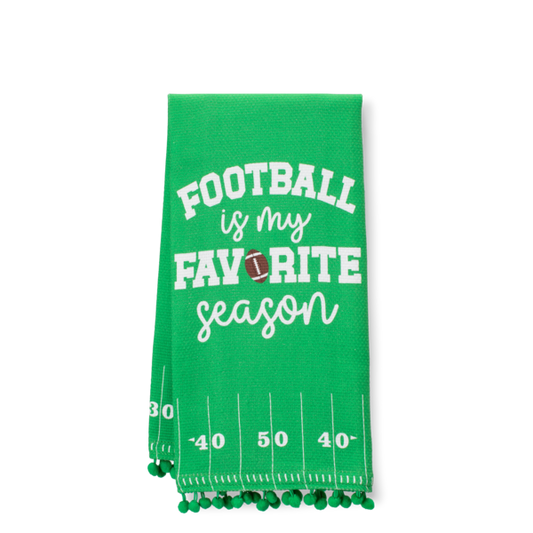 A green kitchen towel with white text reading 'FOOTBALL is my FAVORITE season' and a small football graphic, featuring yard line numbers and green pom-pom trim along the edge.