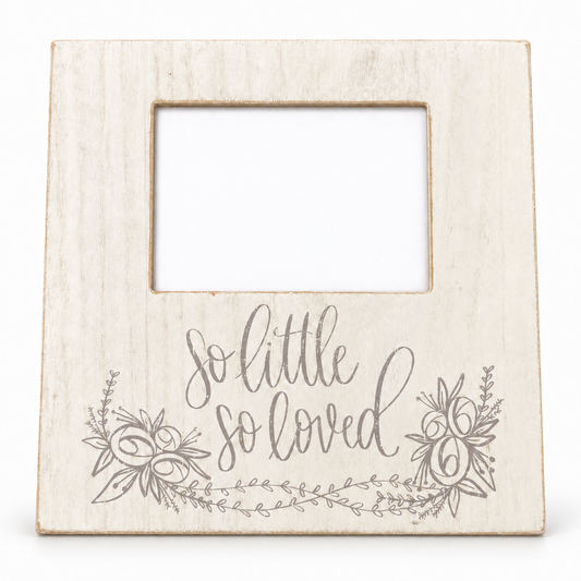 A square, rustic off-white wooden picture frame with a central cutout and the phrase 'so little so loved' in gray script, decorated with gray floral illustrations at the bottom, shown on a plain white background.
