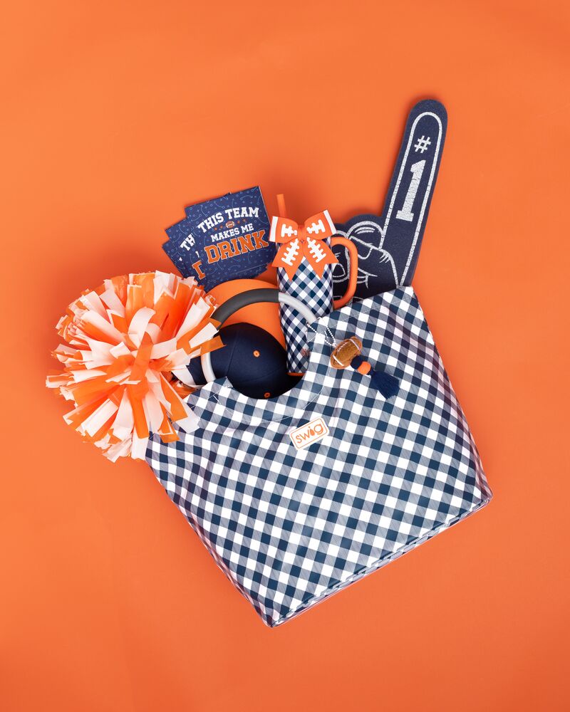 A gingham tote bag filled with gameday collegiate football party accessories, arranged on a solid orange background. auburn.