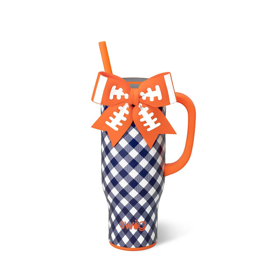 A navy and white gingham patterned tumbler with an orange handle, orange rim, and an orange straw. It features a large orange bow on top with white football lace details and the word 'SWIG' printed in orange near the bottom. Auburn University fans.