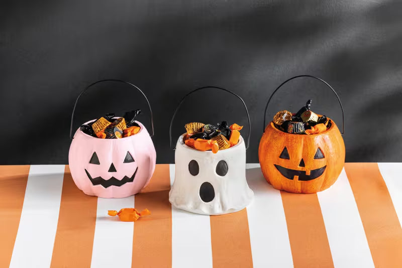Three Halloween-themed candy buckets on a striped tablecloth with a blackboard background.