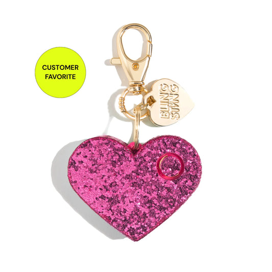 A pink glitter heart-shaped safety alarm keychain with a gold clasp, a small gold heart charm engraved with 'BLING STING', and a bright yellow-green circular badge that reads 'CUSTOMER FAVORITE' on a white background.