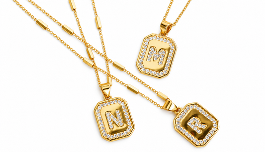 gold initial necklace with square pendant charms displaying the letter N embellished with clear pavé stones, arranged on a clean white background.