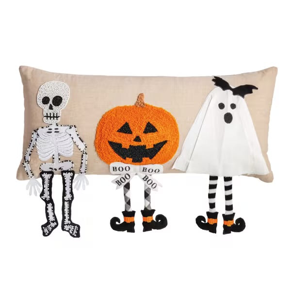Decorative pillow with Halloween-themed characters including a skeleton, pumpkin, and ghost on a beige background.