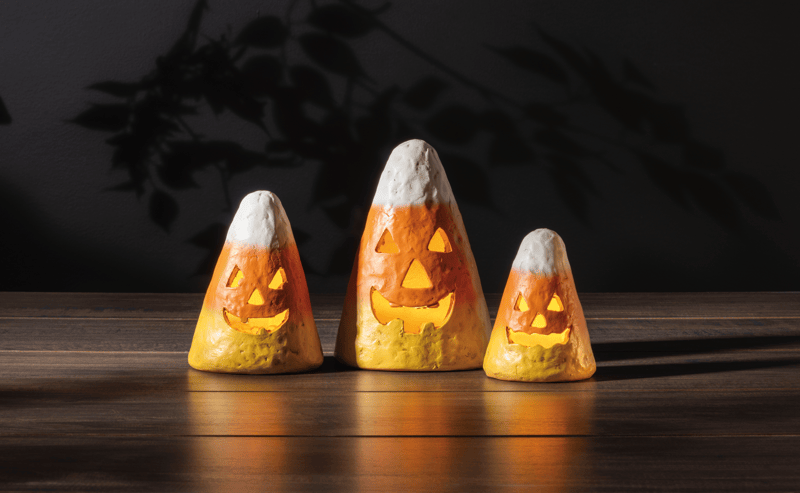Three candy corn-shaped Halloween lights on a wooden surface with a dark background