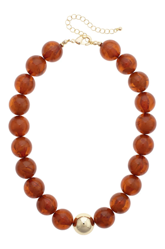 A beaded necklace made of round amber-brown beads with a single polished gold bead at the front, connected by a gold-tone chain extender and clasp, shown on a plain white background.
