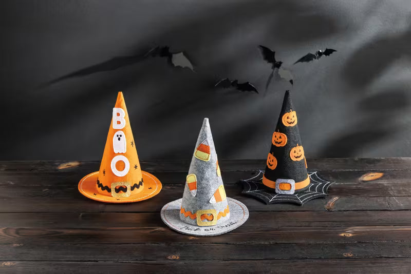 Three Halloween-themed hats on a wooden surface with a dark background and bats.