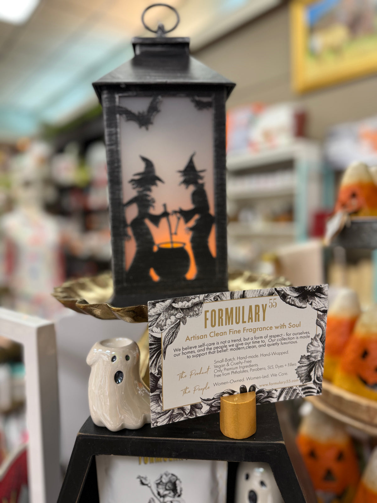 A Halloween lantern with a distressed black metal frame and skeleton cutouts, featuring a warm pinkish-orange glow from within, shown on a plain white background.