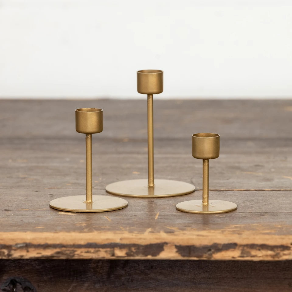 Three brass candlesticks of different heights arranged on a rustic wooden surface against a light background.