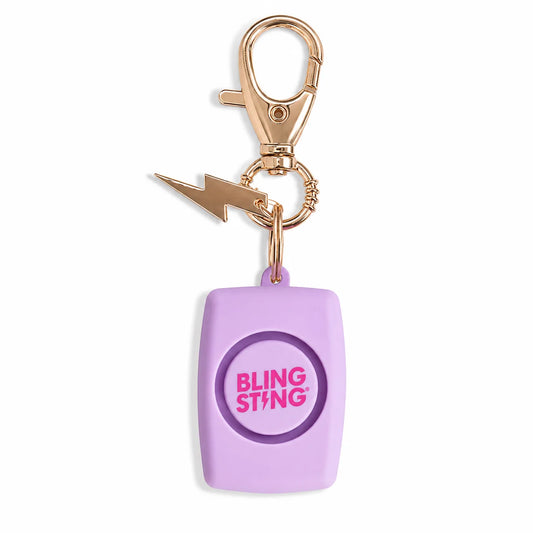 A purple rectangular safety alarm keychain with a gold-tone lobster clasp and lightning bolt charm. The alarm features a circular button with the pink text 'BLING STING' on a clean white background.