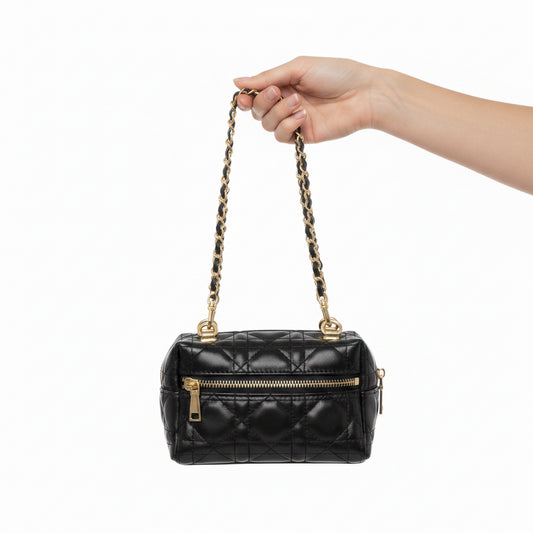 A hand holding a black quilted leather shoulder bag with a gold-tone chain strap and gold zipper, shown against a plain white background.