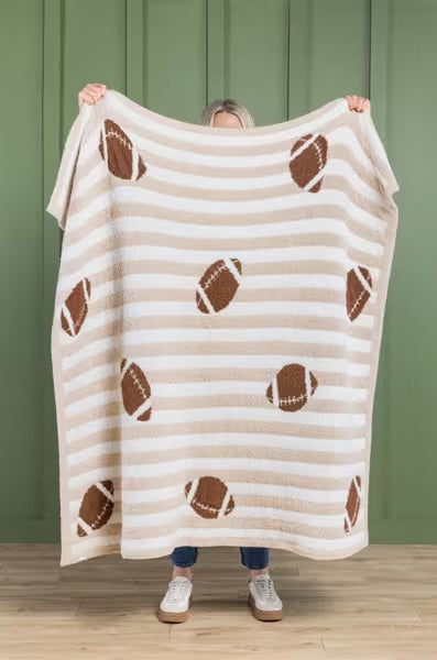 Person holding a striped blanket with football patterns against a green wall.