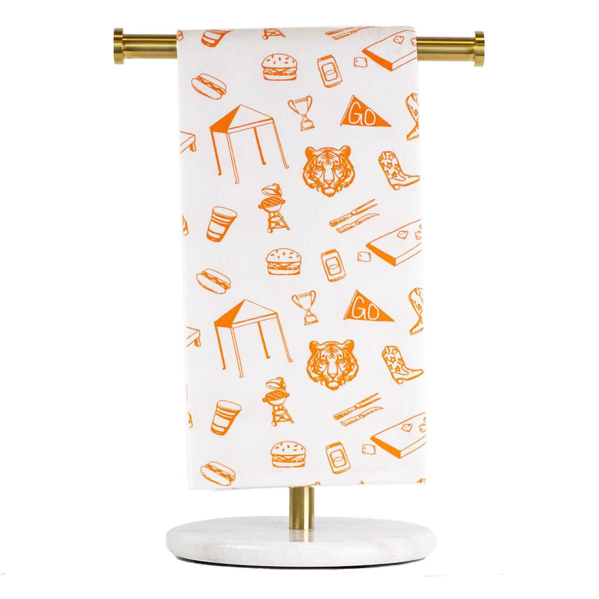 A white kitchen towel with an orange outline pattern of sports and food icons, hanging from a gold metal bar on a marble and gold stand against a white background.  Auburn University, Tigers, War Eagle, Football, Tailgate.