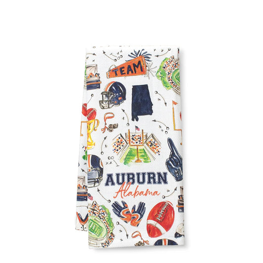 A folded white kitchen towel featuring a colorful Auburn University 'Team' print with illustrations of football helmets, a football, a trophy, a field goal, and the words 'Auburn Alabama'.