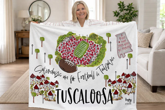 Person holding a blanket with football and Tuscaloosa design in a living room.