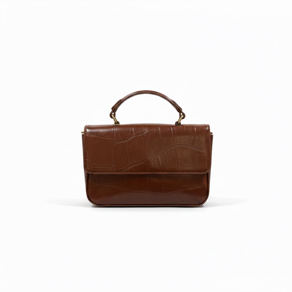 A brown leather handbag with a crocodile-embossed texture on the front flap and a glossy finish on the lower body, featuring a top handle and gold-tone hardware, set against a plain white background.