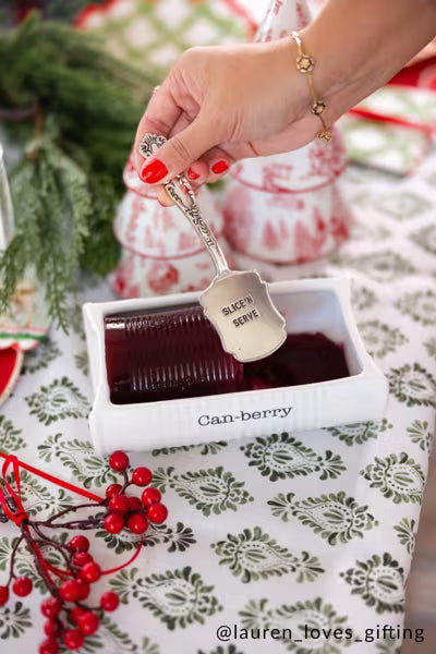 2-piece Cranberry serving dish set  with serving dish and spatula. Cranberry serving dish features debossed sentiment that reads "Can-berry". vintage style spatula reads "slice n' serve".  Christmas table scene.